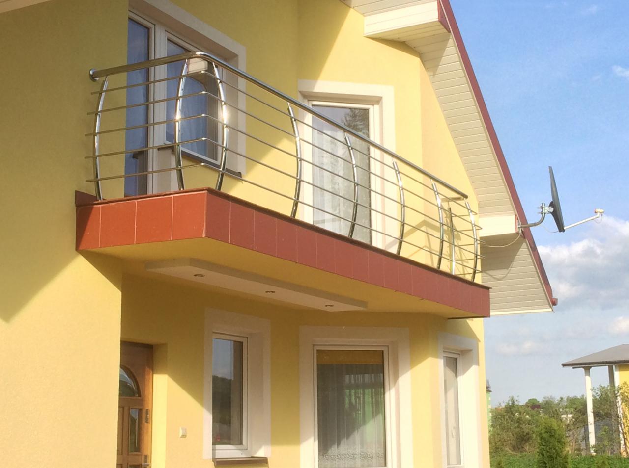 Balkon z chromowaną balustradą o zaokrąglonych elementach, wykończony czerwoną płytką, na tle żółtej elewacji domu z widoczną anteną satelitarną.