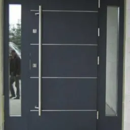 Grafitowe drzwi wejściowe z przeszkleniami i długim uchwytem, nowoczesny design. Realizacja w Zielonce.