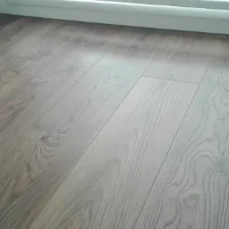 Ułożone panele podłogowe w odcieniach brązu, widoczne łączenia i struktura drewna, blisko białej listwy przypodłogowej.