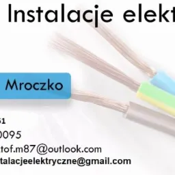 Reklama firmy elektrycznej: Trzy żyły kabla elektrycznego w kolorach niebieskim, zielono-żółtym i szarym na białym tle, obok nazwa firmy K&M - Instalacje elektryczne, imię i nazwisko Krzysztof...