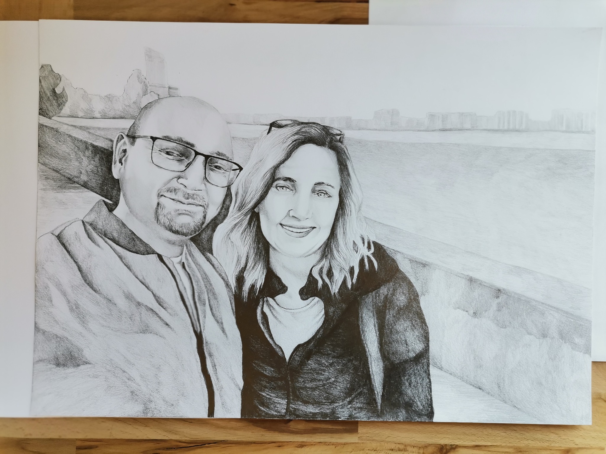 Portret pary narysowany ołówkiem, z widokiem na miasto w tle.