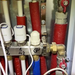 Elektro-start Jakub Popławski - Rozdzielacz ogrzewania podłogowego z termostatami Salus, rury w izolacji czerwonej i niebieskiej, widoczne zawory i przewody.