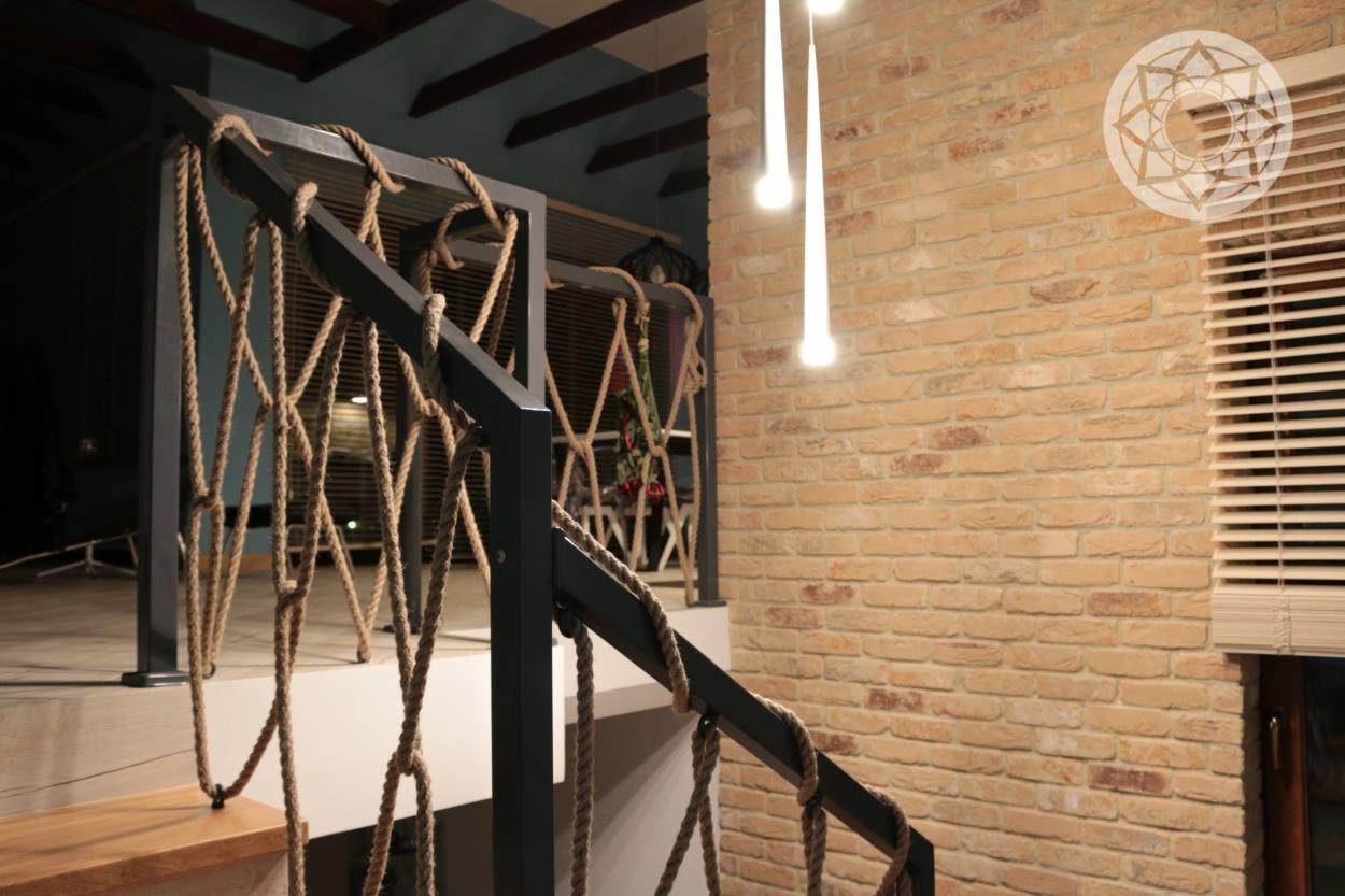 Schody z balustradą z czarnego metalu i dekoracyjną liną jutową, ceglana ściana w tle, nowoczesne lampy wiszące