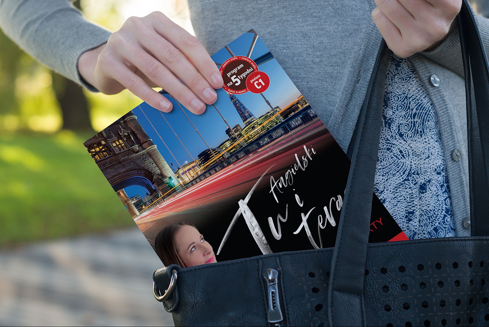 Kobieta wkłada do czarnej torebki broszurę reklamową z nocnym widokiem na Tower Bridge i napisem 'Angielski w tera'.