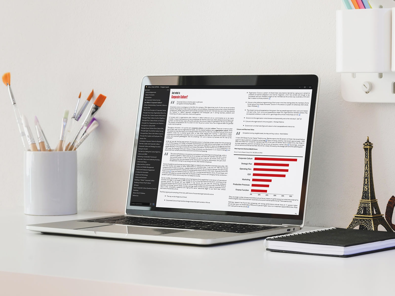 Laptop displaying a document titled 'Just what is Corporate Culture?' with a bar graph showing 'Corporate Culture' as the most important value driver, alongside paintbrushes in a white container...