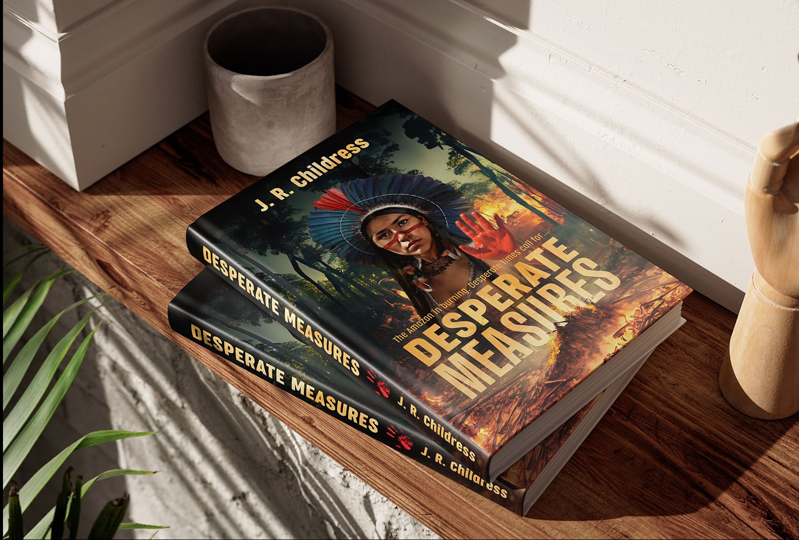Dwa egzemplarze książki 'Desperate Measures' J.R. Childress ułożone na drewnianym stole, z okładką przedstawiającą kobietę w tradycyjnym nakryciu głowy na tle płonącego lasu deszczowego.