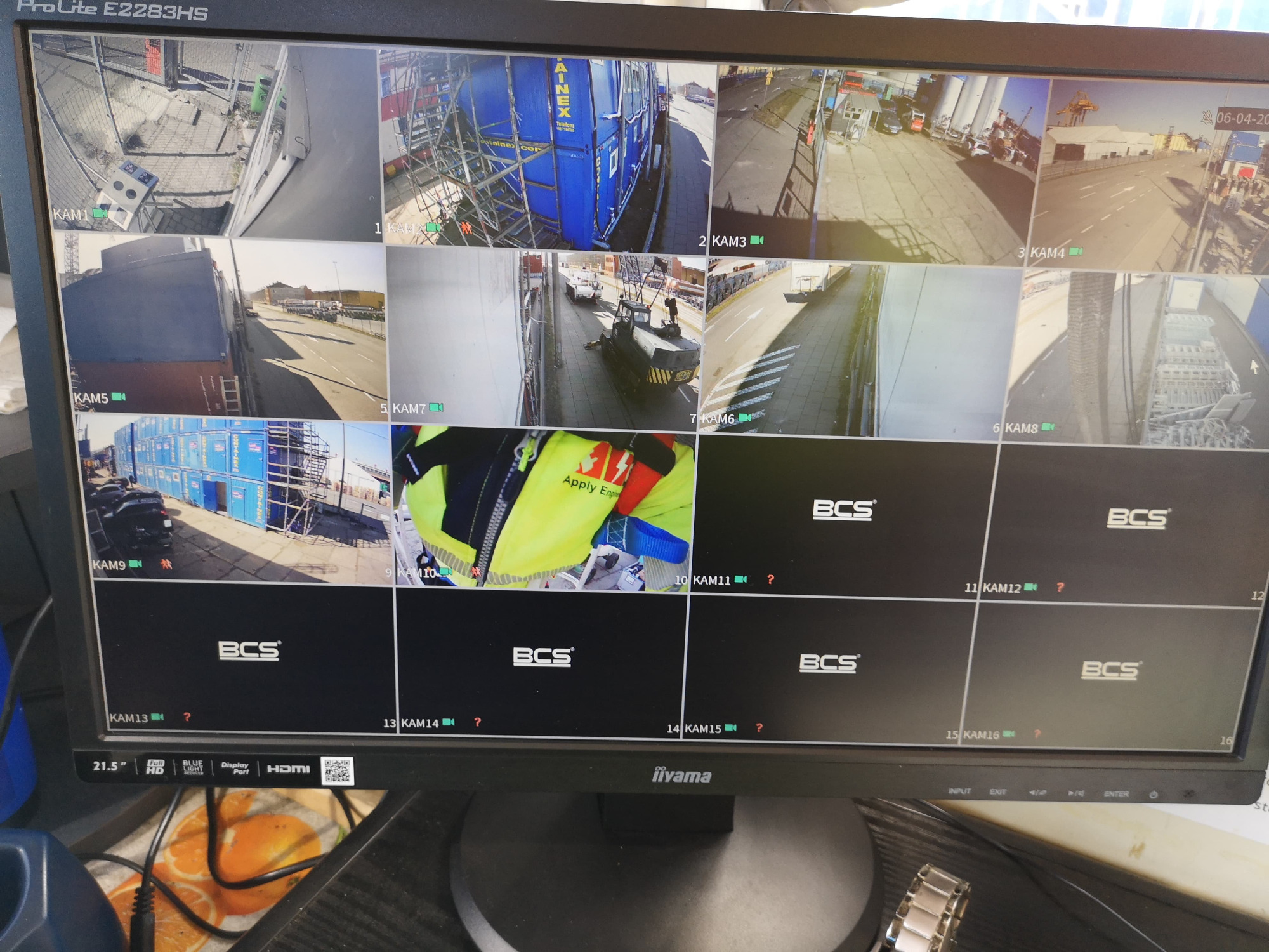 Monitor z widokiem z wielu kamer przemysłowych na plac budowy, magazyn kontenerowy i prace na wysokościach.