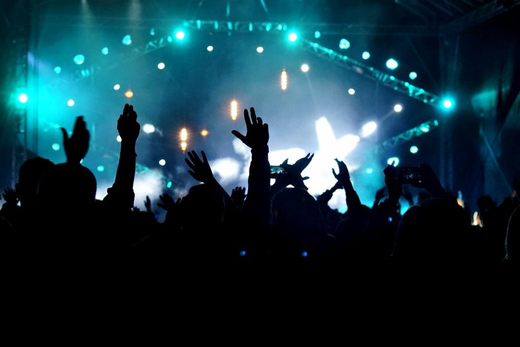 Tłum ludzi z podniesionymi rękami w ciemności, oświetlony niebieskimi i białymi światłami sceny podczas koncertu.