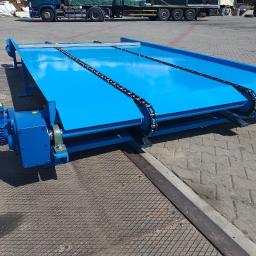 Turmet - Niebieski, stalowy przenośnik łańcuchowy z silnikiem elektrycznym, widoczny na zewnątrz na tle zaparkowanej ciężarówki.