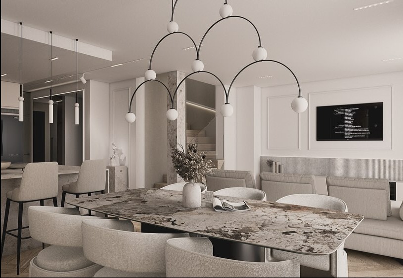 Jasne wnętrze jadalni z marmurowym stołem, krzesłami w odcieniach beżu i oryginalną lampą. W tle widoczna kuchnia i schody, całość w minimalistycznym stylu.