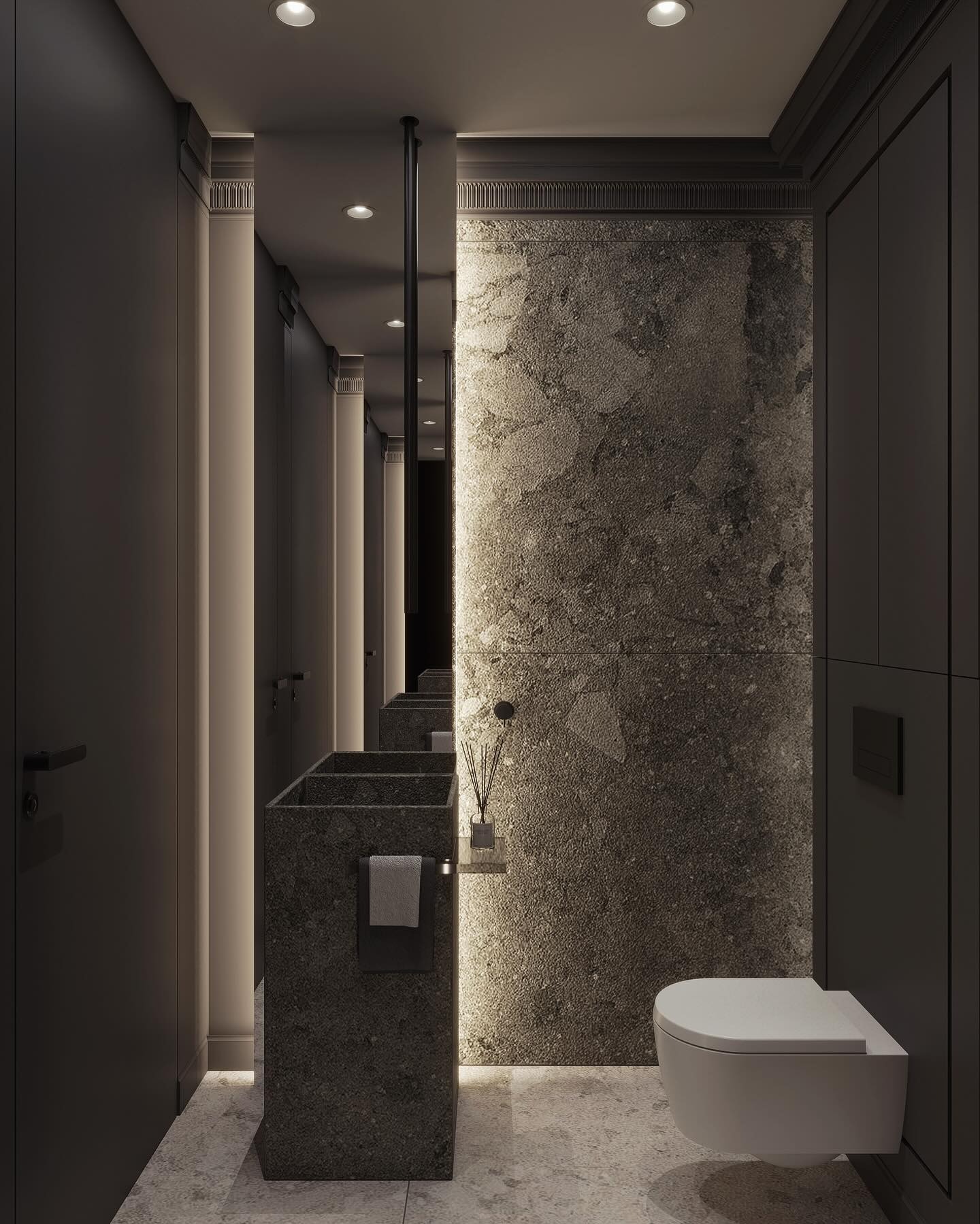 Elegancka, ciemna łazienka z kamienną umywalką, lustrem i toaletą podwieszaną. Minimalistyczny design z akcentami dekoracyjnymi i subtelnym oświetleniem.