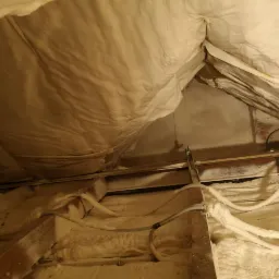 Poddasze po izolacji, widoczne drewniane elementy konstrukcyjne i przewody pokryte warstwą pianki. W tle fragment ściany z widoczną starą boazerią.