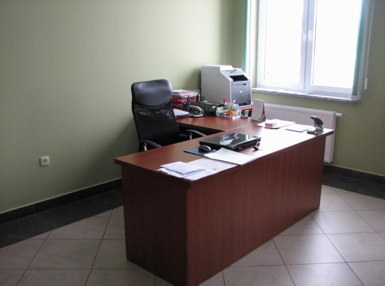 Biuro z biurkiem, krzesłem, laptopem i drukarką przy oknie, oświetlonym naturalnym światłem.