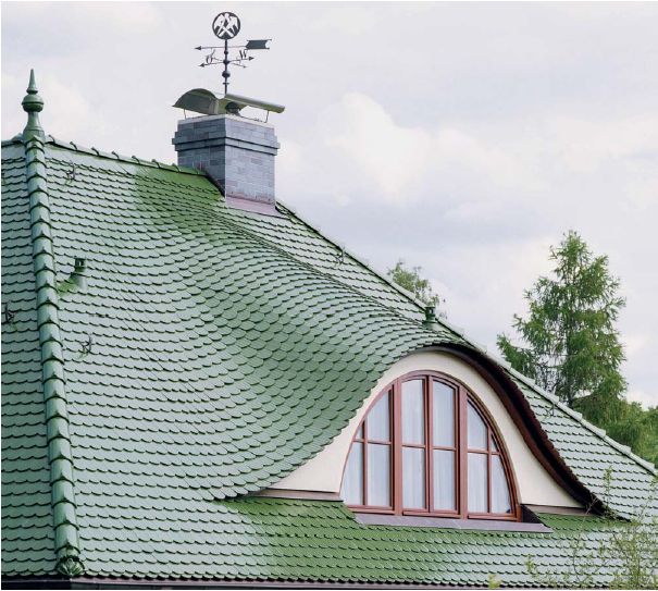 Zielony dach kryty łuską z okrągłym oknem na poddaszu i wiatrowskazem z symbolem górniczym na kominie.