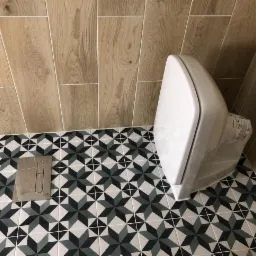 Nowoczesna łazienka z płytkami podłogowymi w geometryczny wz&oacute;r gwiazdy i drewnopodobnymi płytkami ściennymi, z widocznym białym kompaktem WC marki Koło.