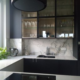 BergerDesign - Nowoczesna kuchnia z czarnymi szafkami i blatem z białego marmuru. Nad blatem szafki z przeszklonymi drzwiami, w których widoczne są szklanki i naczynia.