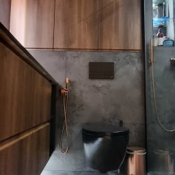 BergerDesign - Nowoczesna łazienka z wiszącą toaletą w kolorze czarnym, armaturą w odcieniach miedzi i drewnianymi szafkami. Na podłodze beżowy dywanik.
