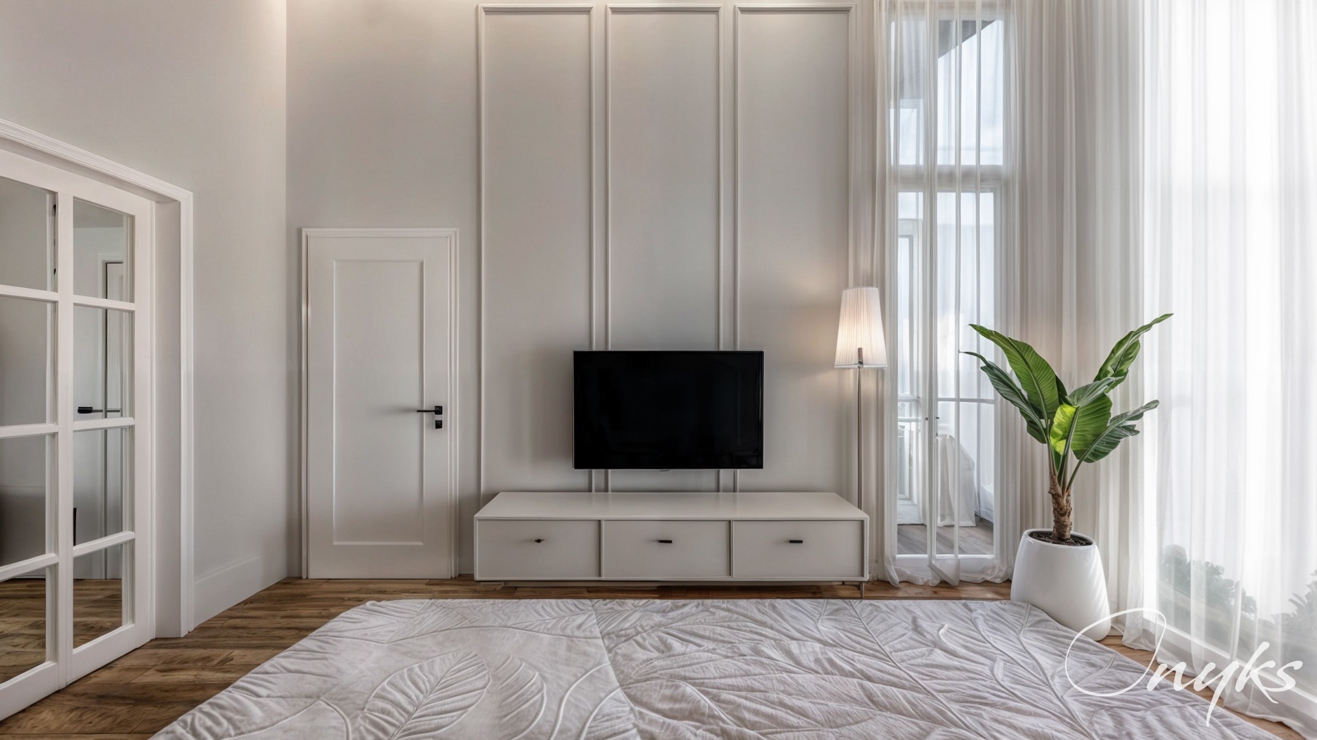 Jasne wnętrze salonu z minimalistycznym umeblowaniem: biała szafka RTV pod wiszącym telewizorem, wysoka lampa podłogowa, roślina doniczkowa i wzorzysty dywan na drewnianej podłodze.