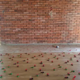 Proces układania płytek podłogowych z użyciem poziomujących klipsów i klinów, widoczna ściana wyłożona cegłą, worek z zaprawą klejową i młotek gumowy.