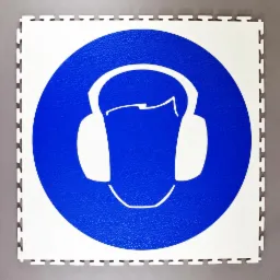 Biała, modułowa posadzka przemysłowa z niebieskim symbolem nakazu noszenia ochronników słuchu.