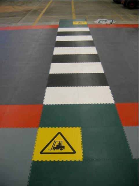 Modułowa podłoga przemysłowa z pasem bezpieczeństwa dla wózków widłowych i znakiem ostrzegawczym.