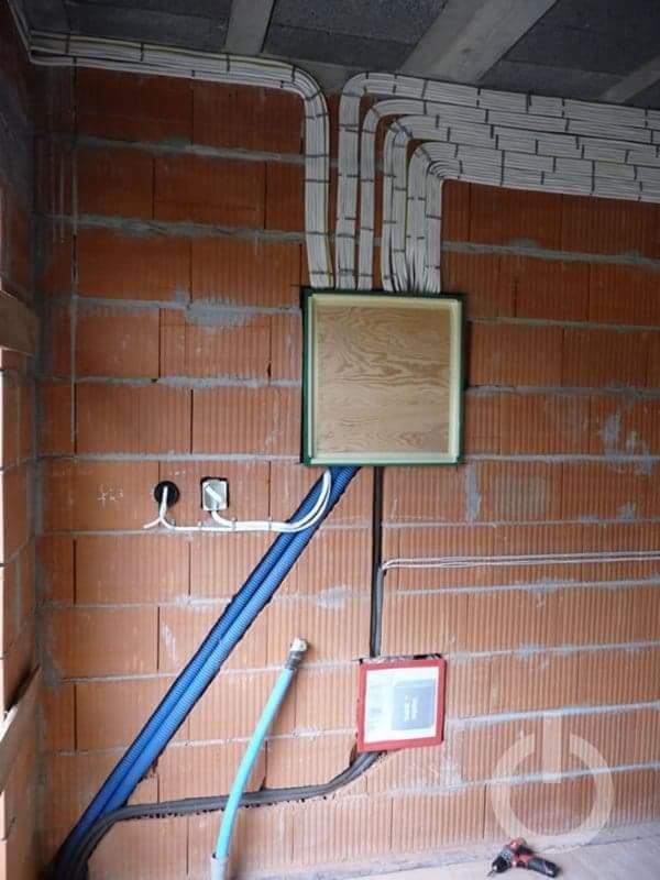 Wewnętrzna instalacja elektryczna w trakcie montażu w surowym budynku z cegły, widoczne kable prowadzone po ścianach i pod sufitem, puszki elektryczne i fragment wiertarki akumulatorowej na podłodze.