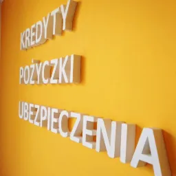Napisy przestrzenne na żółtej ścianie: Kredyty, Pożyczki, Ubezpieczenia.