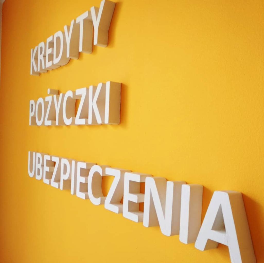 Napisy przestrzenne na żółtej ścianie: Kredyty, Pożyczki, Ubezpieczenia.