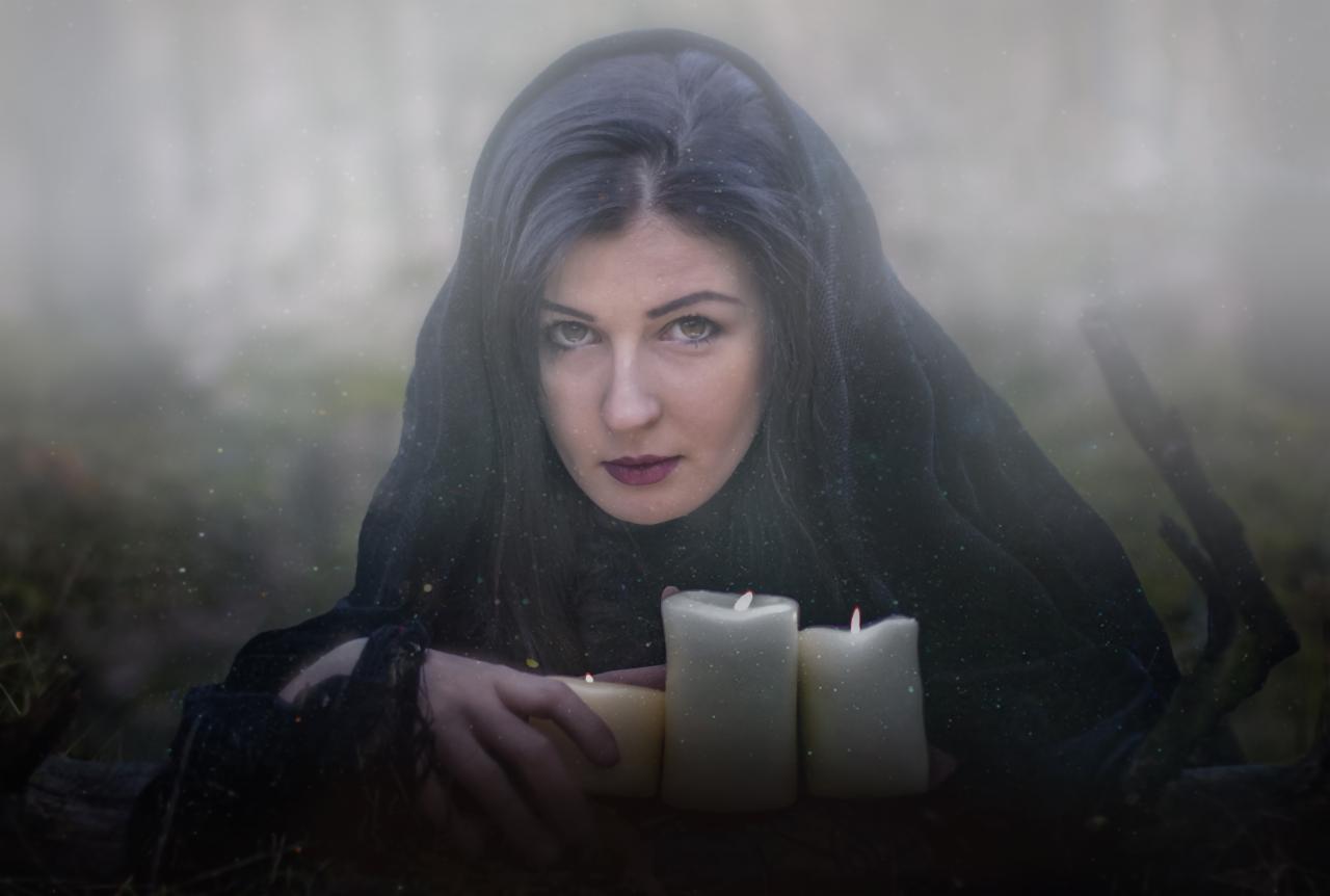 Portret kobiety z ciemnymi włosami w czarnej chuście, trzymającej zapalone świece w leśnym otoczeniu, z efektem mgły i delikatnymi iskierkami.