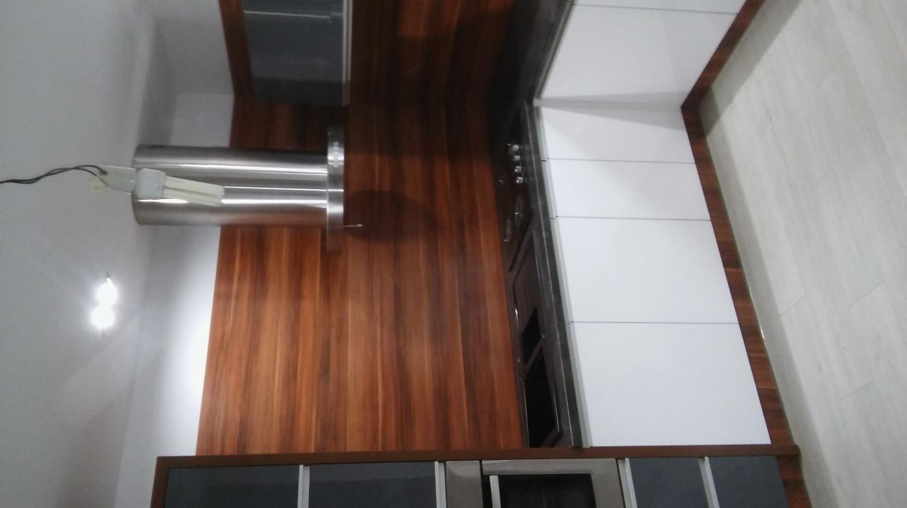 Nowoczesna kuchnia z białymi szafkami i drewnianym panelem ściennym, oświetlona lampą halogenową, widok z góry.