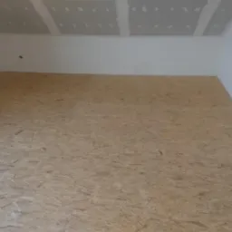 Poddasze z wyłożoną płytą OSB na podłodze, ściany częściowo wykończone płytami gipsowo-kartonowymi, widoczne łączenia płyt.