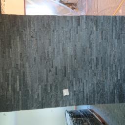 Usługi remontowo-budowlane - Fragment ściany wykończonej czarnym kamieniem dekoracyjnym z widocznym gniazdkiem elektrycznym i zabezpieczeniem podłogi folią malarską.