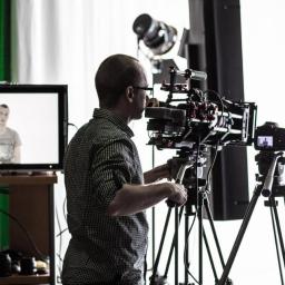 Agencja Flipside - Produkcja filmów, reklam i animacji - Operator kamery w okularach obsługuje profesjonalny sprzęt filmowy w studio, z widocznym monitorem podglądowym i oświetleniem.