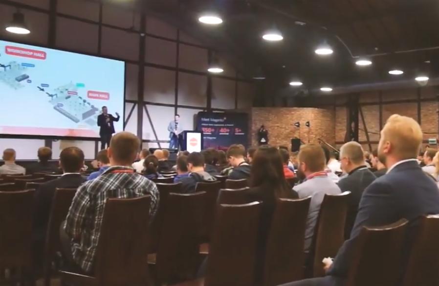 Prezentacja na konferencji z widoczną sceną, ekranem z diagramem i publicznością siedzącą na krzesłach.