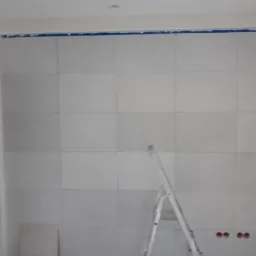 Ściana wyłożona płytami w Sobieszynie, przygotowana do dalszych prac wykończeniowych, z widoczną drabiną i zabezpieczeniem taśmą malarską przy suficie.