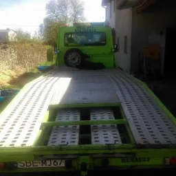 Zielona laweta Renault z numerem telefonu na kabinie, zaparkowana obok budynku z drabiną.