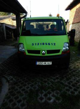 Jasnozielony bus Renault z numerem telefonu i tablicą rejestracyjną SBE MJ67, zaparkowany pod zadaszeniem, z widocznymi antenami na dachu.