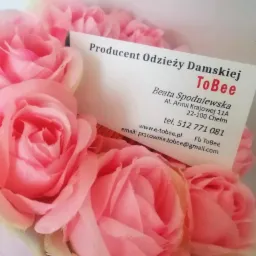 Wizytówka producenta odzieży damskiej ToBee, umieszczona wśród bukietu różowych róż, prezentująca dane kontaktowe: adres, telefon, e-mail i adres strony internetowej.