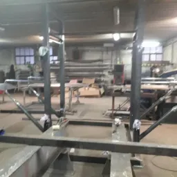 Wnętrze warsztatu z konstrukcją stalową w trakcie budowy, widoczne elementy spawane i przygotowane do montażu, w tle osoba w roboczym ubraniu.