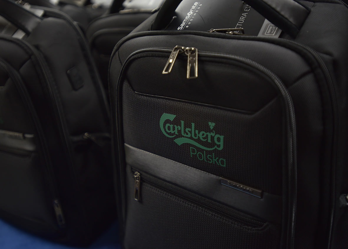Czarne plecaki biznesowe z nadrukowanym zielonym logo Carlsberg Polska, ustawione w rzędzie.