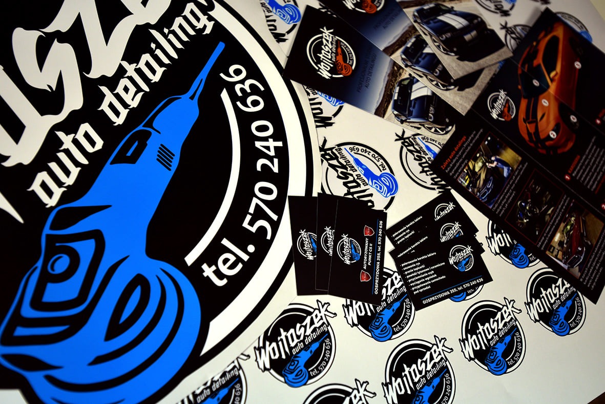 Stos wizytówek, naklejek i ulotek reklamowych z logo firmy auto detailingowej Wojtaszek, prezentujących ofertę usług i dane kontaktowe.