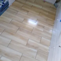 Ułożone jasne płytki imitujące drewno na podłodze, widoczne krzyżyki dystansowe, świeżo po montażu, częściowo ułożone płytki na ścianie.