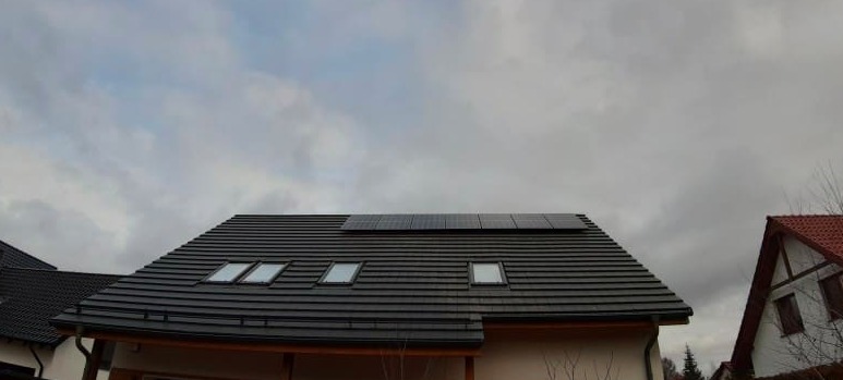 Czarny dach z dachówkami ceramicznymi i oknami połaciowymi, na którym zamontowano panele słoneczne w pochmurny dzień.