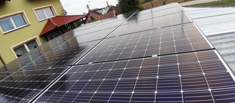 Panele słoneczne na dachu domu jednorodzinnego, widoczne okna i dach budynku w tle.