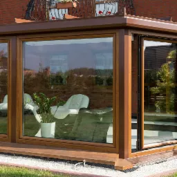 Zadaszony taras z brązową ramą okienną, wyposażony w białe fotele i dekoracyjny wazon z motywem zebry, widoczny przez otwarte przesuwne drzwi.