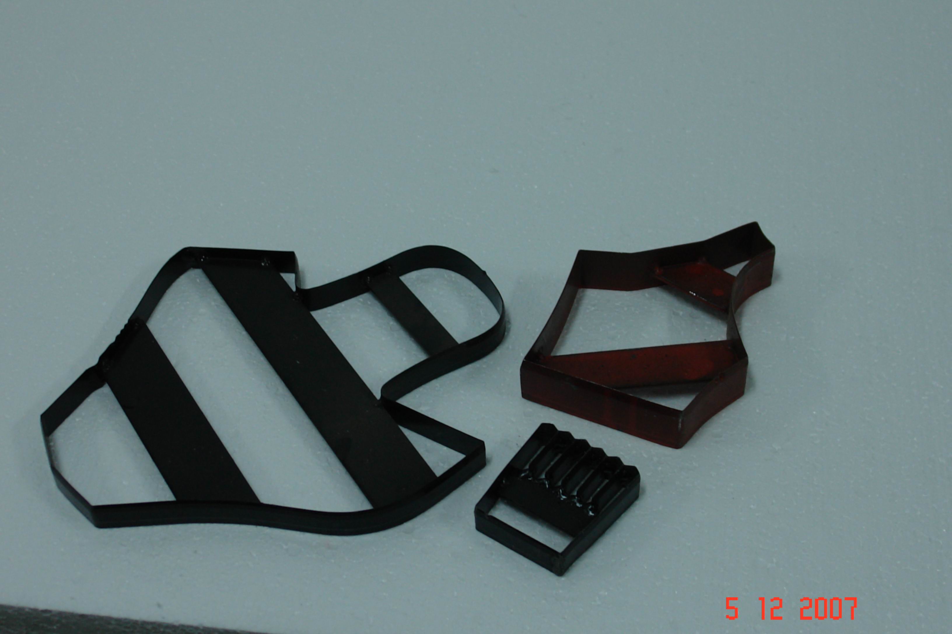 Zestaw wykrojników cholewkarskich: duży, stalowy wykrojnik z ukośnymi pasami, średni wykrojnik w kształcie tarczy oraz mały wykrojnik z ząbkami, ułożone na szarym tle.