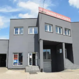 Szary budynek firmy z szyldem 'Energy Gaz Polska' na dachu, widoczne wejście, okna i brama garażowa.