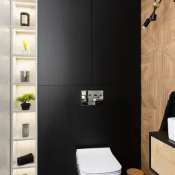 Nowoczesna toaleta w Kaniowie z zabudową meblową w kolorze czarnym i drewnianą ścianą z geometrycznym wzorem, oświetlona półka z dekoracjami i wisząca miska WC.
