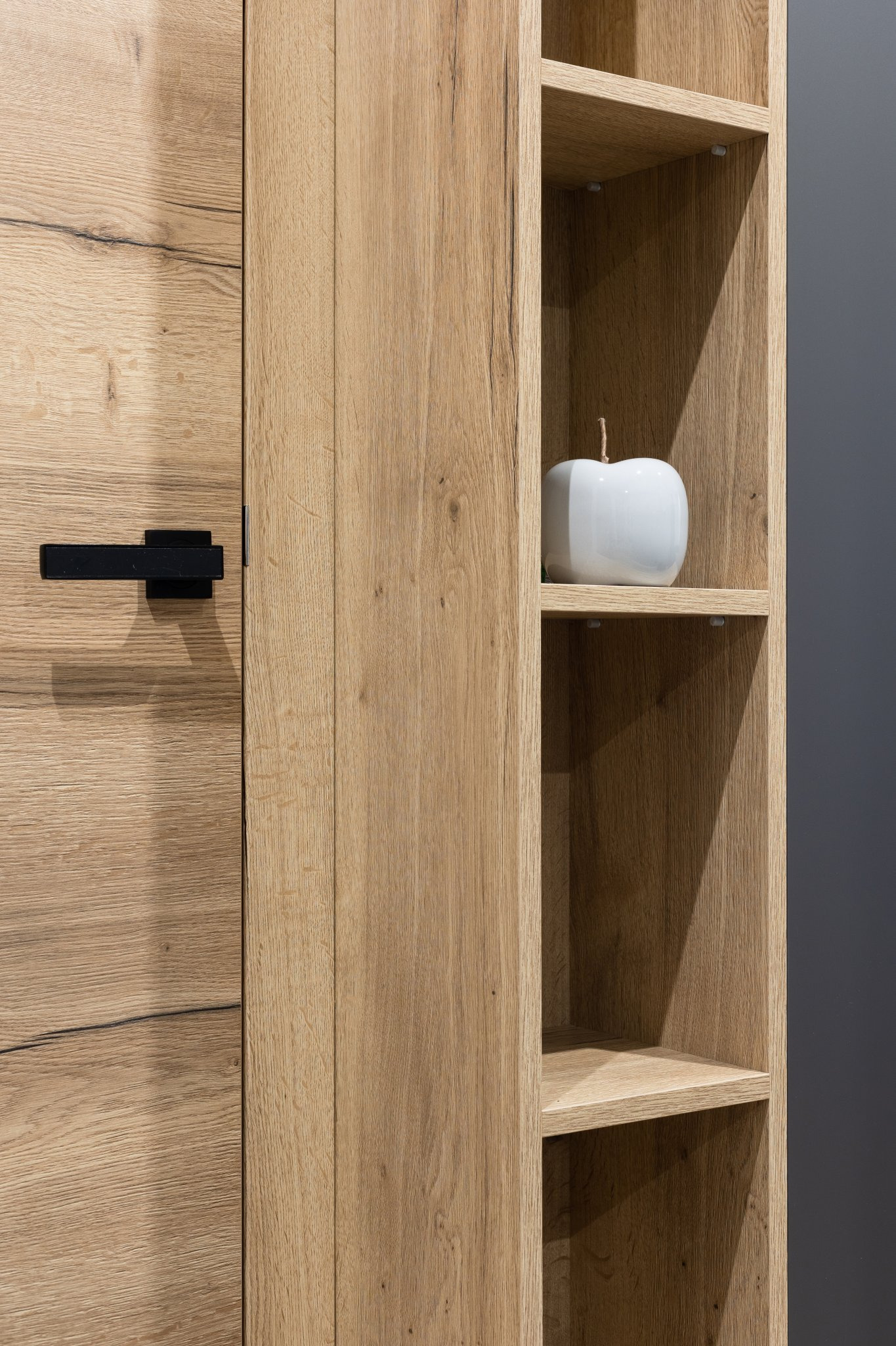 Drewniana szafka kuchenna z czarnym uchwytem i otwartymi półkami z ceramiczną jabłkiem jako dekoracją.