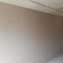 Świeżo położone, gładkie tynki na ścianach w rogu pomieszczenia z surowym betonowym sufitem i wiszącą żarówką.